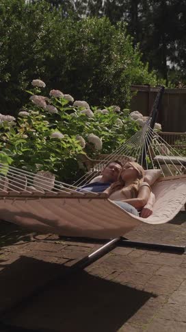 Couple sleeps together in a hammock setup on the paved portion of their backyard