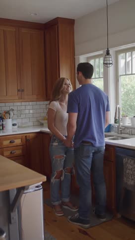 Couple gaze into each others eyes as they hold both hands in the kitchen