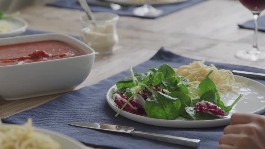 Salad on a plate in front of a dish of marinara sauce being scooped with a wooden spoon