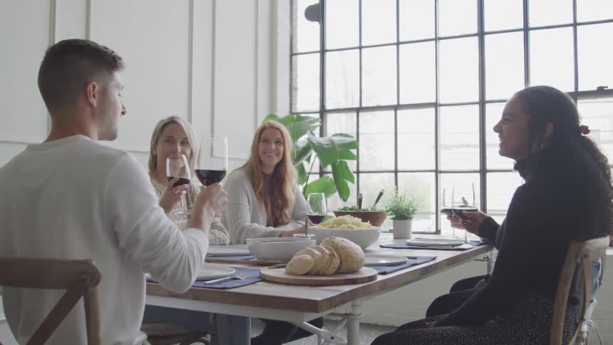 Friends sitting around dining table with wine and food smiling