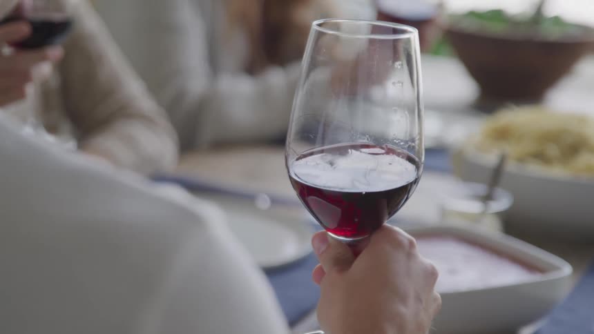 A person holds a glass of red wine at a dining table as others swirl their glasses aerating the wine