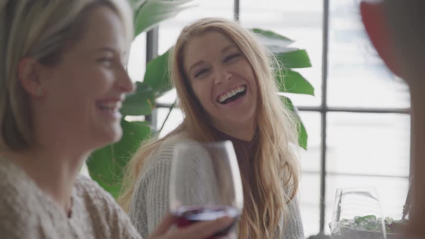 Women are laughing as they sit and drink wine