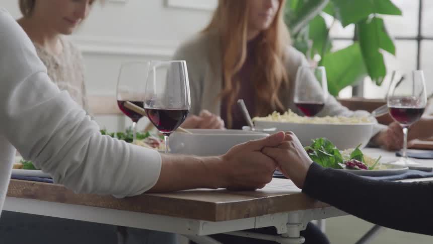 Family joins hands around the table to pray over their meal