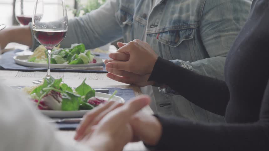 People gathered around table holding hands to say grace before eating