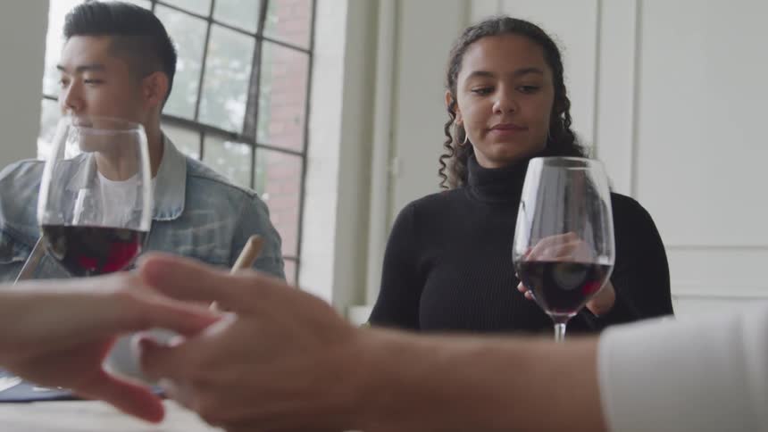 People sitting at a table with food and glasses of wine holding hands to begin a prayer before eating
