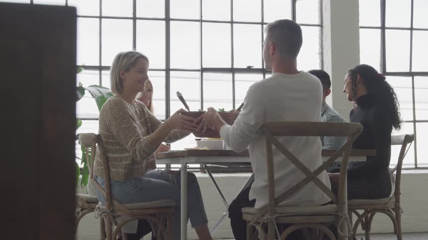 A woman passes the salad at the dining room table