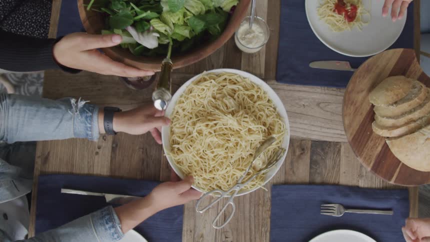 People passing spaghetti and salad around at a dining table