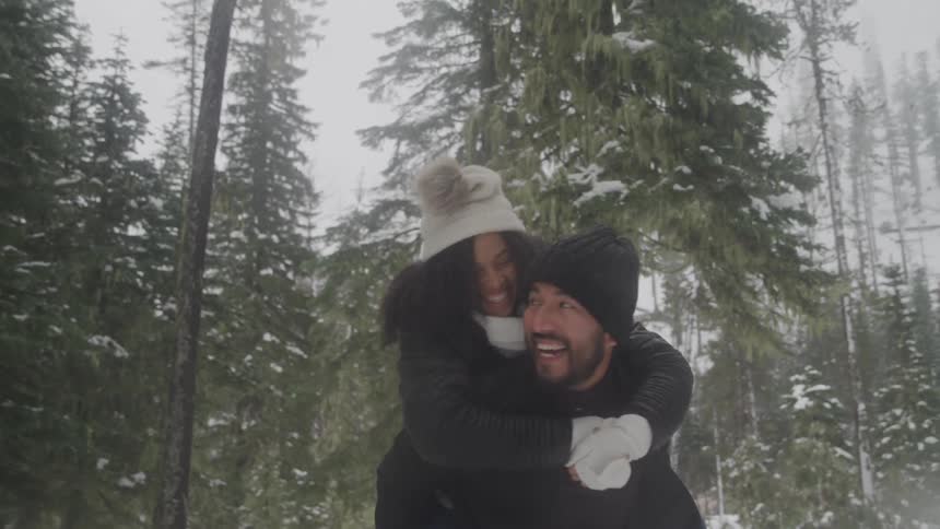 Man gives woman a piggy back ride and spins her around in the forest