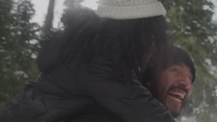 A man is giving a woman a piggy back ride as they laugh and play around outside in the winter