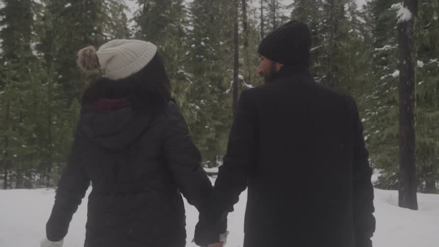 A man and a woman dressed in dark winter clothing walk together in a snowcovered forest