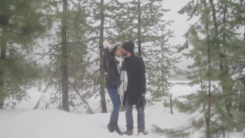 A couple kiss while taking a selfie in the forest