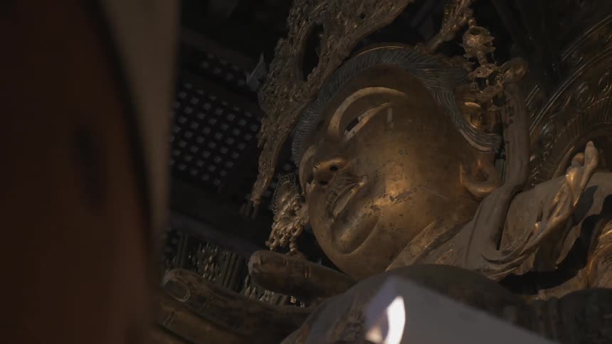 A large buddha with gold color sits in a temple