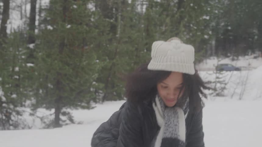 A woman in winter clothes joyfully throws snowballs in a snowy forest
