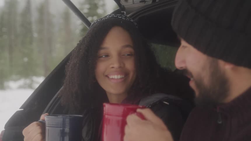 Couple toasting with coffee mugs tailgating from suv in snow covered forest