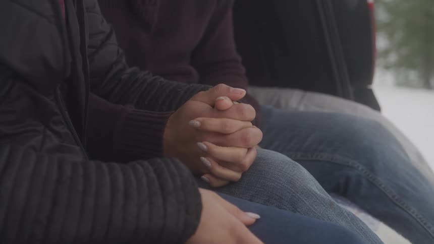 A couple hold hands sitting in the hatch of the car