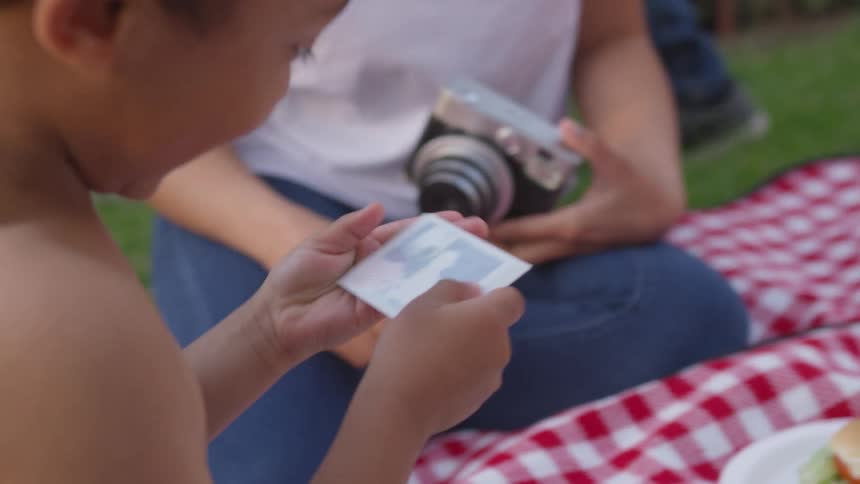 A child looks at a photo while sitting on a picnic blanket