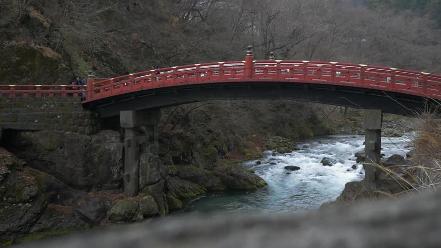 Red arched bridge with a rapidly moving river below it