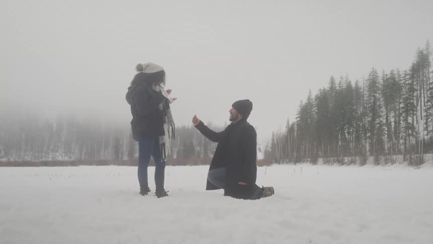 Man getting down on one knee in the snow proposing to his girlfriend
