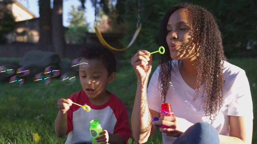 A mother and son are blowing bubbles in the park