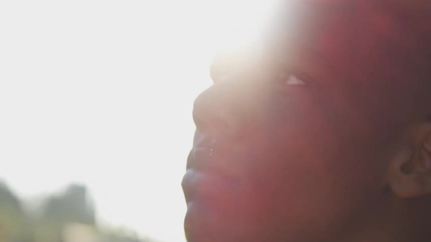 A closeup profile of a man gazing upward sunlight shines brightly behind him