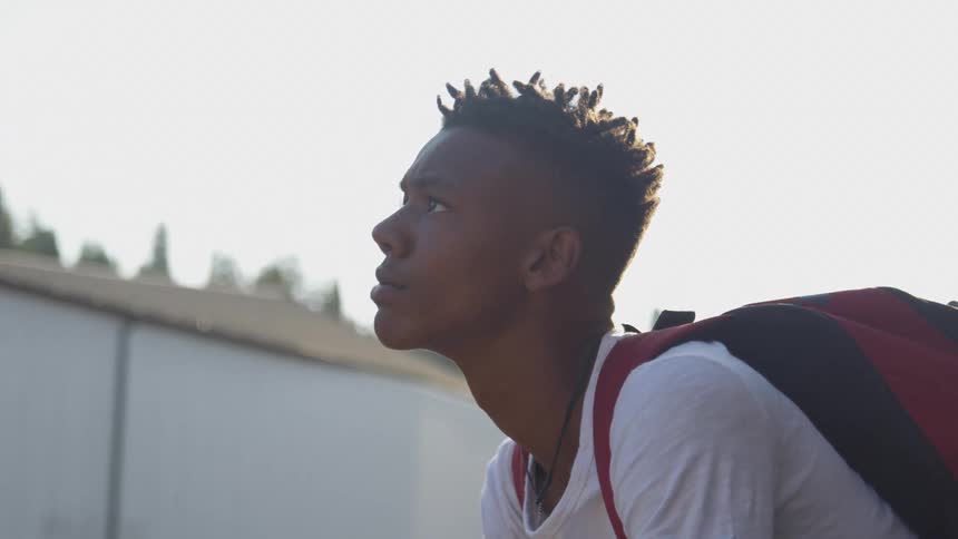 Teenage boy wearing a backpack raises his head to the sky