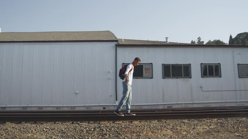 A teenage boy is walking on railroad tracks