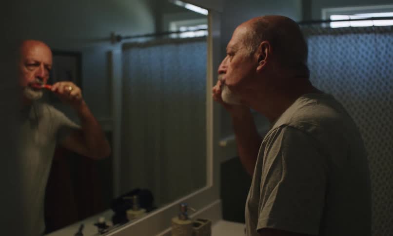 Man brushing his teeth by mirroring himself in the bathroom