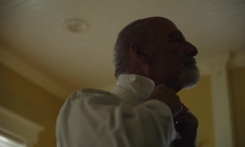 A man puts on a dress shirt and walks away