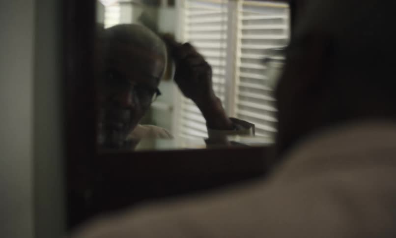 Man brushes then combs his hair while looking in a mirror