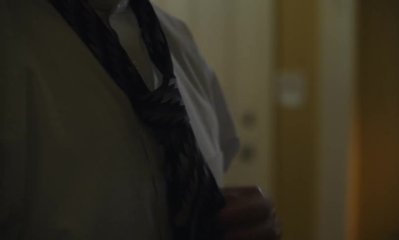 An elderly man is putting a tie on his white suit