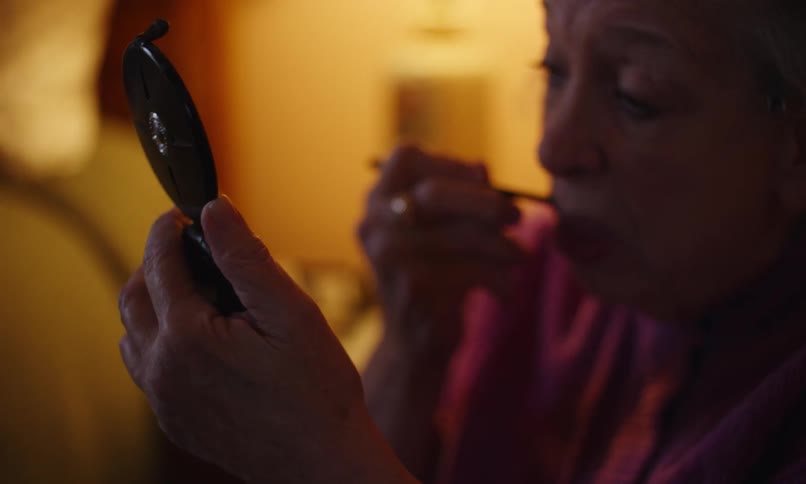 A woman is applying makeup in a small mirror