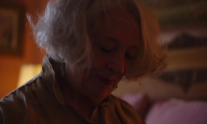An elderly woman is smiling and standing in a room