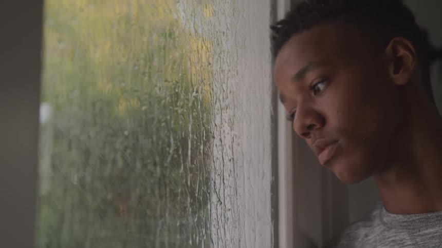 A teenager is watching the rain hit the window
