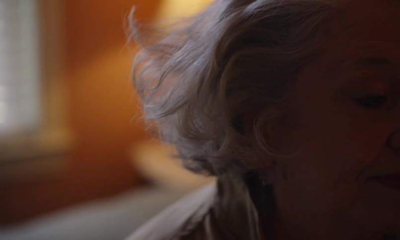 Woman sits on her bed and runs her fingers through her hair