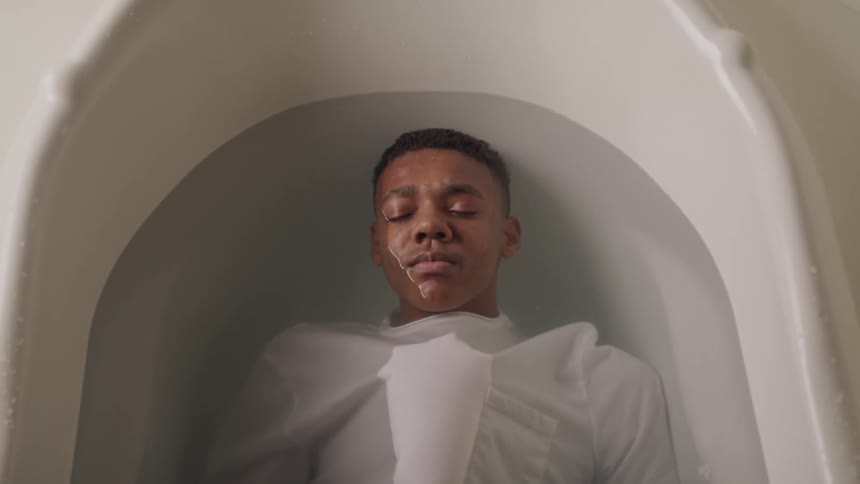 Teenager lies partially submerged in a bathtub while wearing a shirt