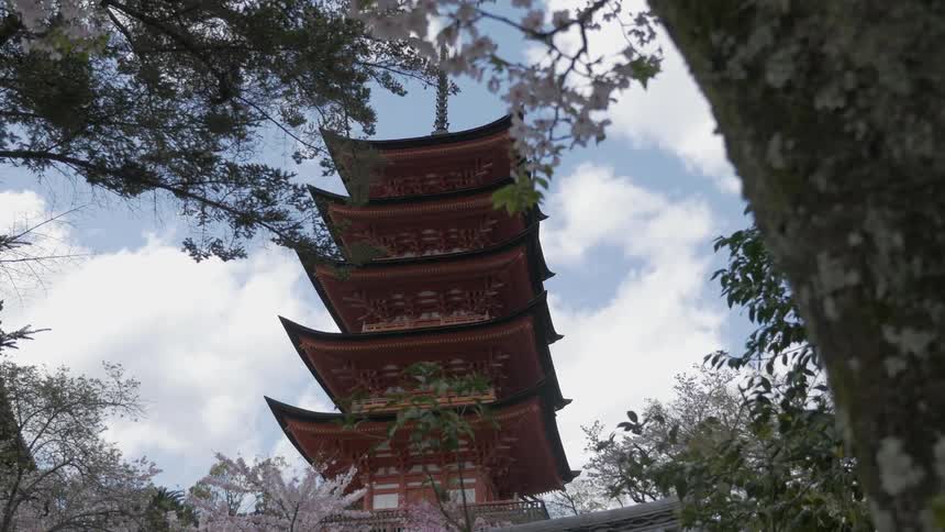 A tall japanese building in front of a cloudy sky with cherry blossom trees