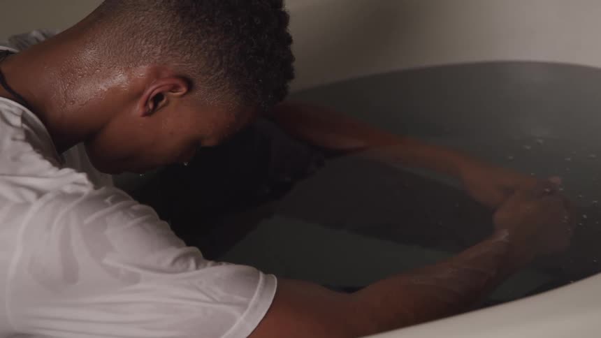 A man is sitting in water in the bathtub while wearing a shirt