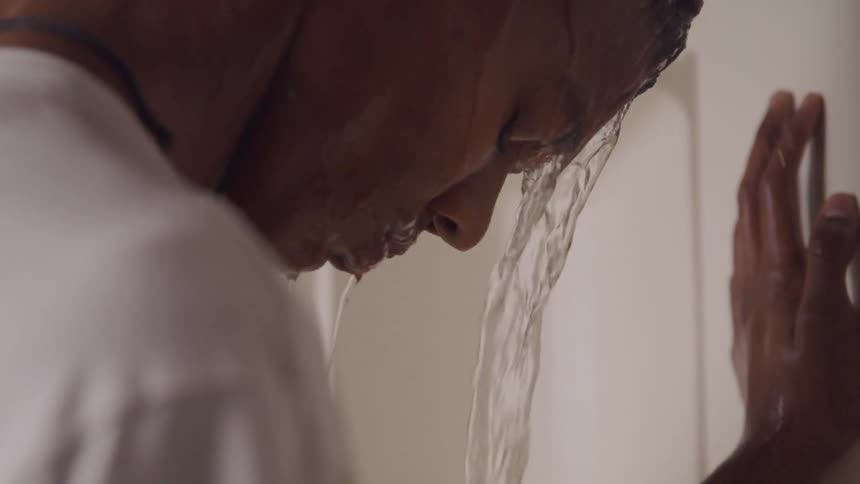 Depressed teenager leaning on shower wall with water running down his face