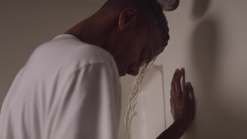 Young adult wears a t shirt while standing under the running shower