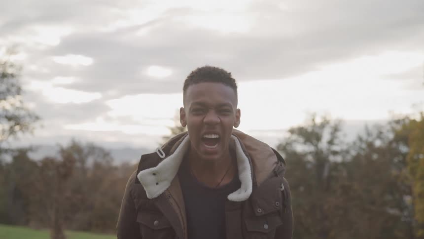 Older teen boy bends slightly as he yells in front of trees