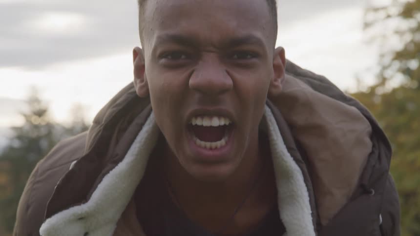 The young black man is looking directly at the camera and screaming as loud as he can