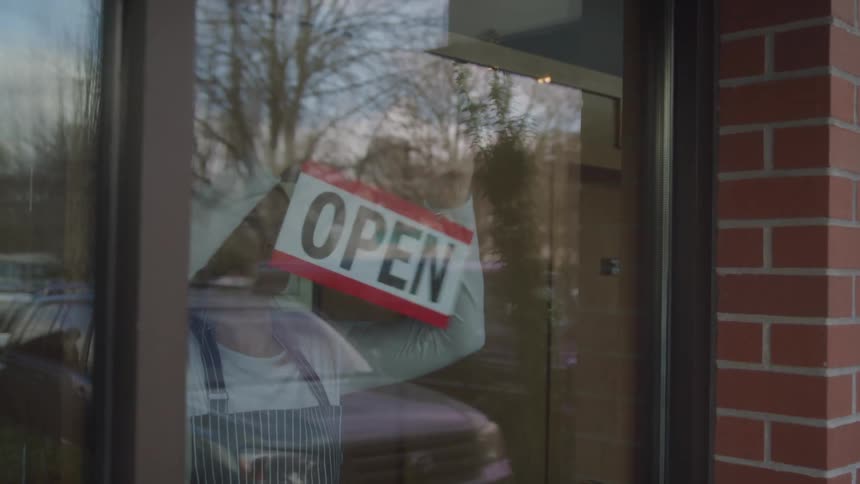 A woman flips a sign from closed to open in the window of a shop