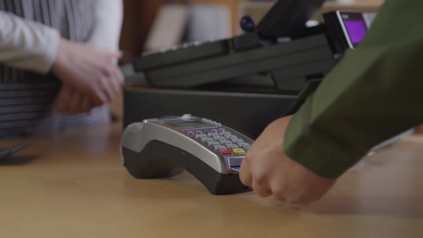 A customer swipes a credit card in a machine at a retail counter with a register