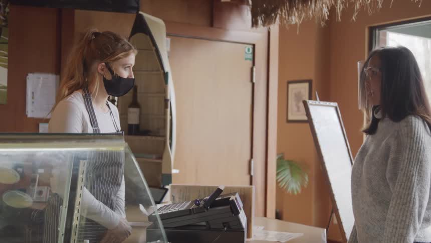 Woman approaches the cash register and talks to another woman behind it