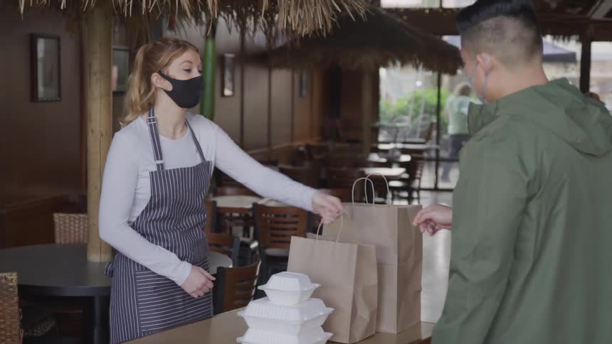 Employee hands a paper bag to a customer in a cafe