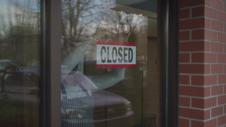 Employee turning open sign to closed inside a business