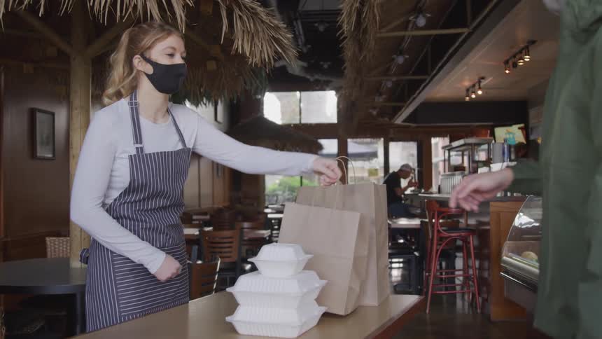 Woman hands a paper bag to a customer in a cafe