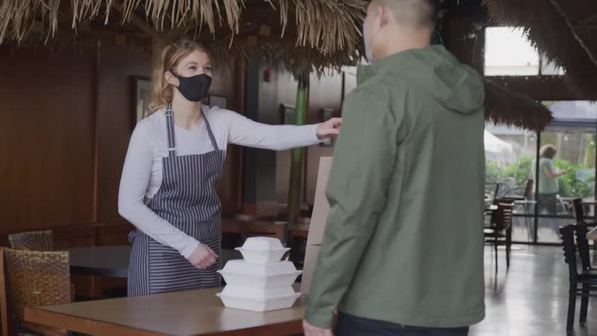 Woman hands a paper bag to a customer before they wave at each other