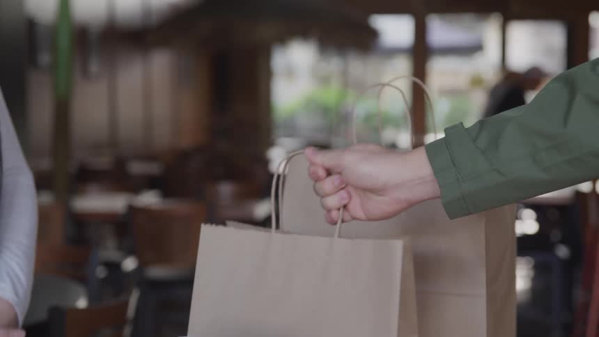 Male customer picks up the takeout bag pointed to by restaurant employee