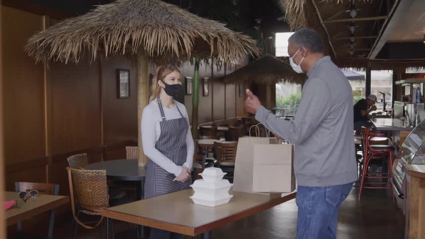 Man picks up a to go order from an employee in a cafe